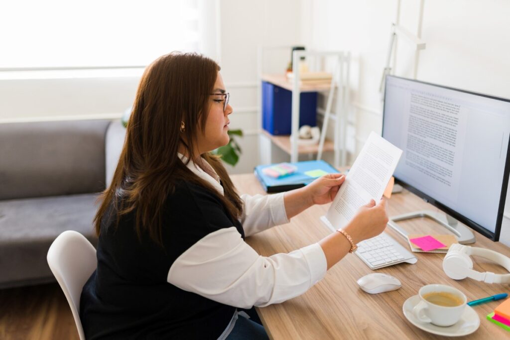 Woman reading some papers in front of a computer.